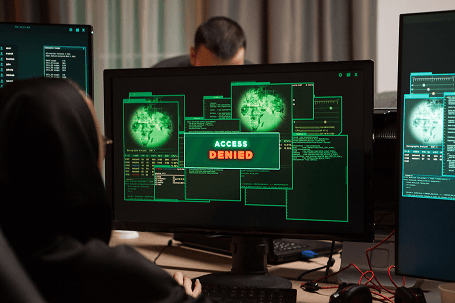 persoon achter computer met scherm waarop een DDoS-aanval wordt weergegeven, inclusief 'Access Denied' melding